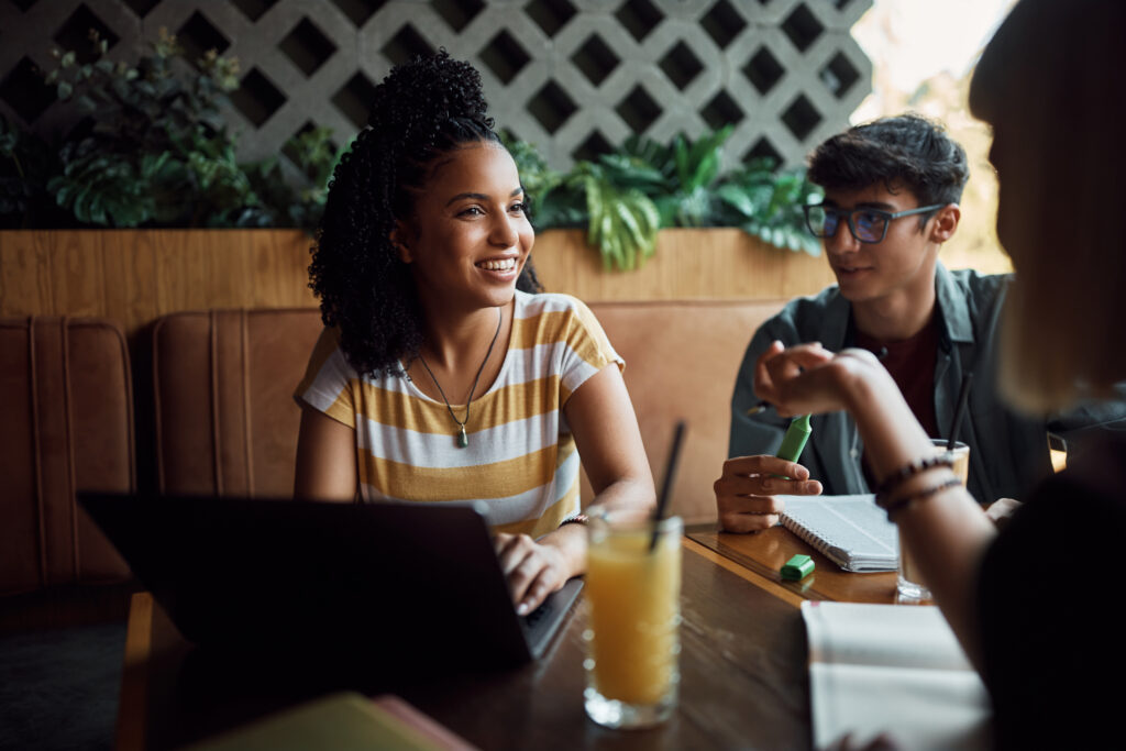 Happy black student using laptop while learning with her friends in a cafe,