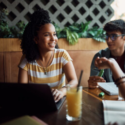 Happy black student using laptop while learning with her friends in a cafe,